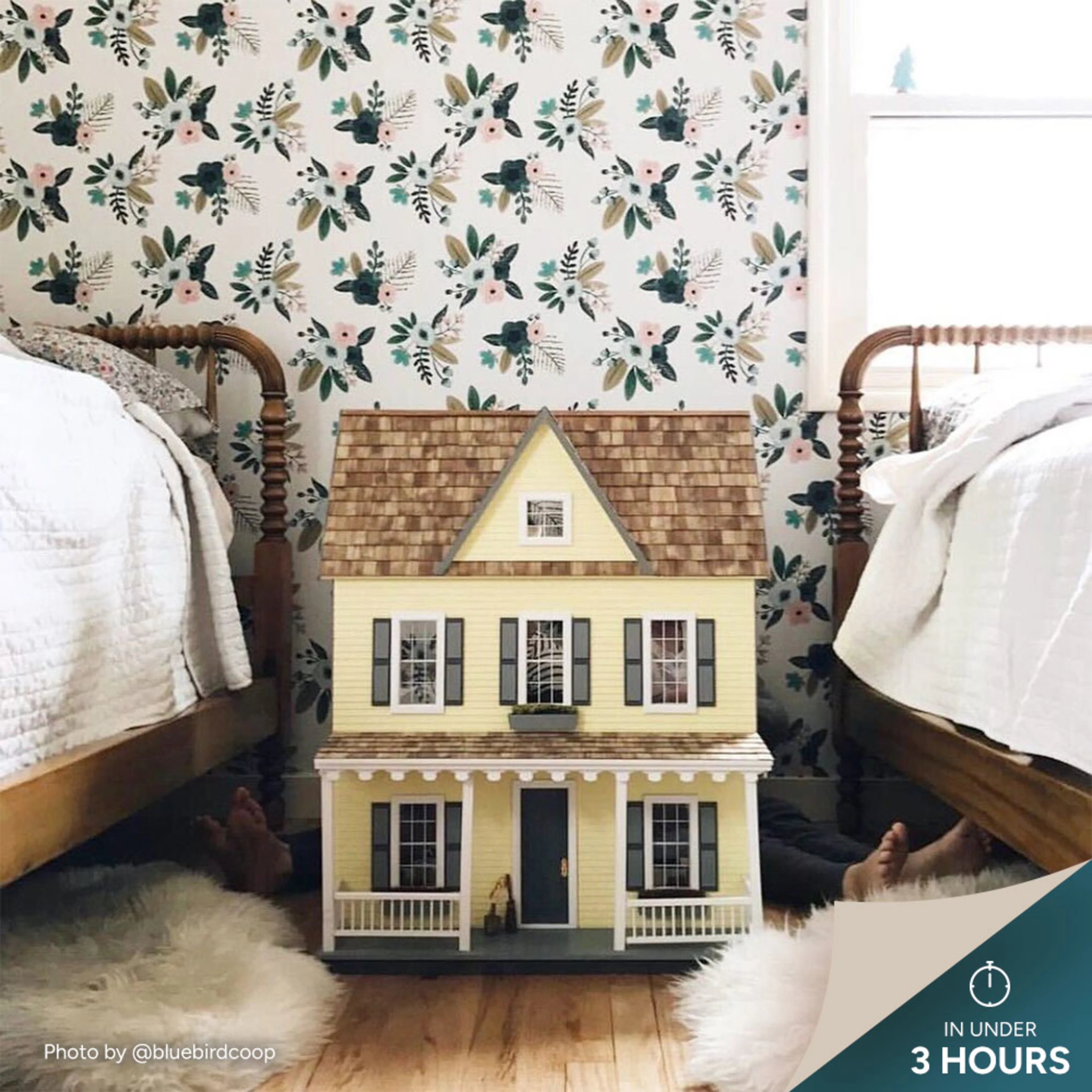 Dollhouse between two beds with floral wallpaper.