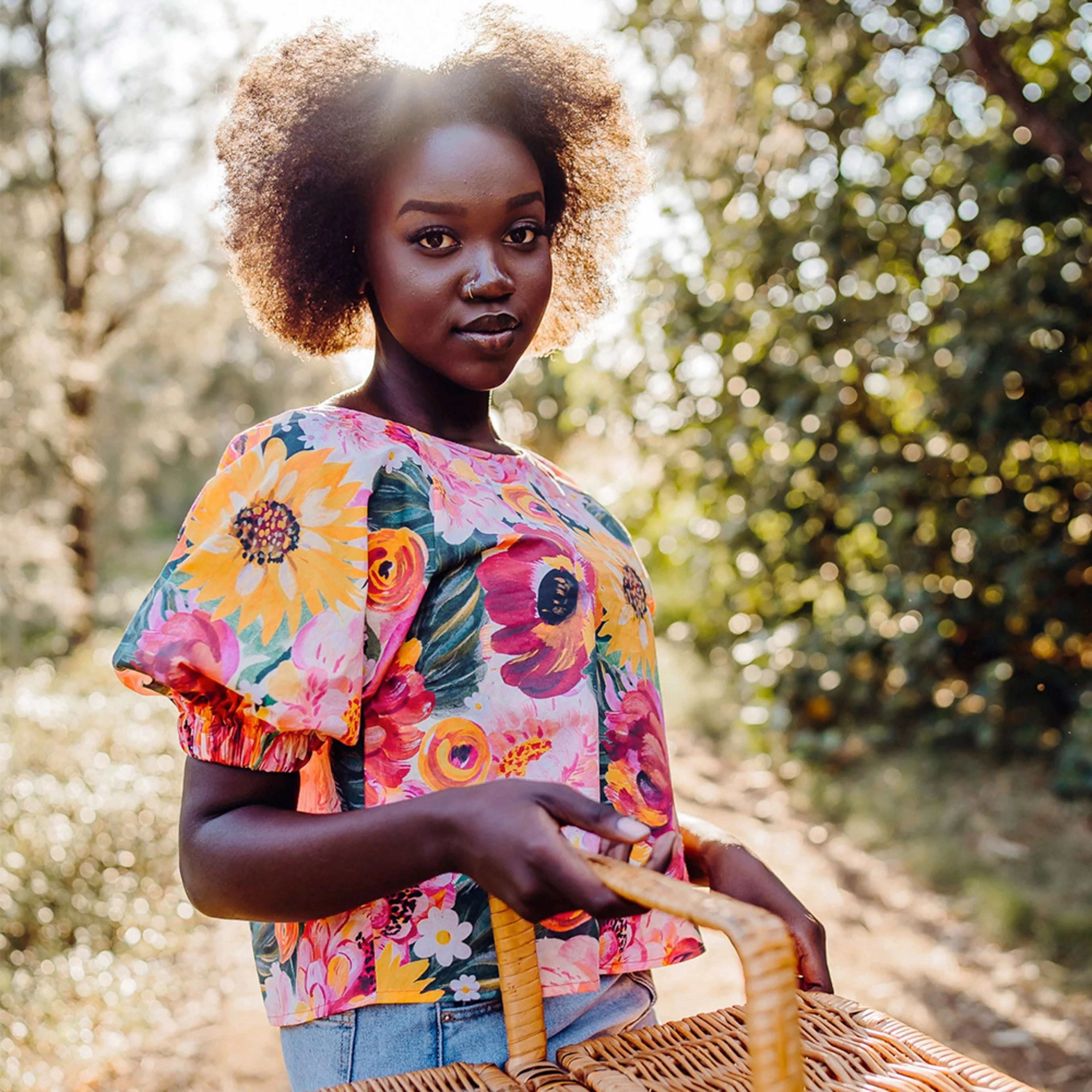 Woman in a floral blouse carrying a picnic basket in the woods.