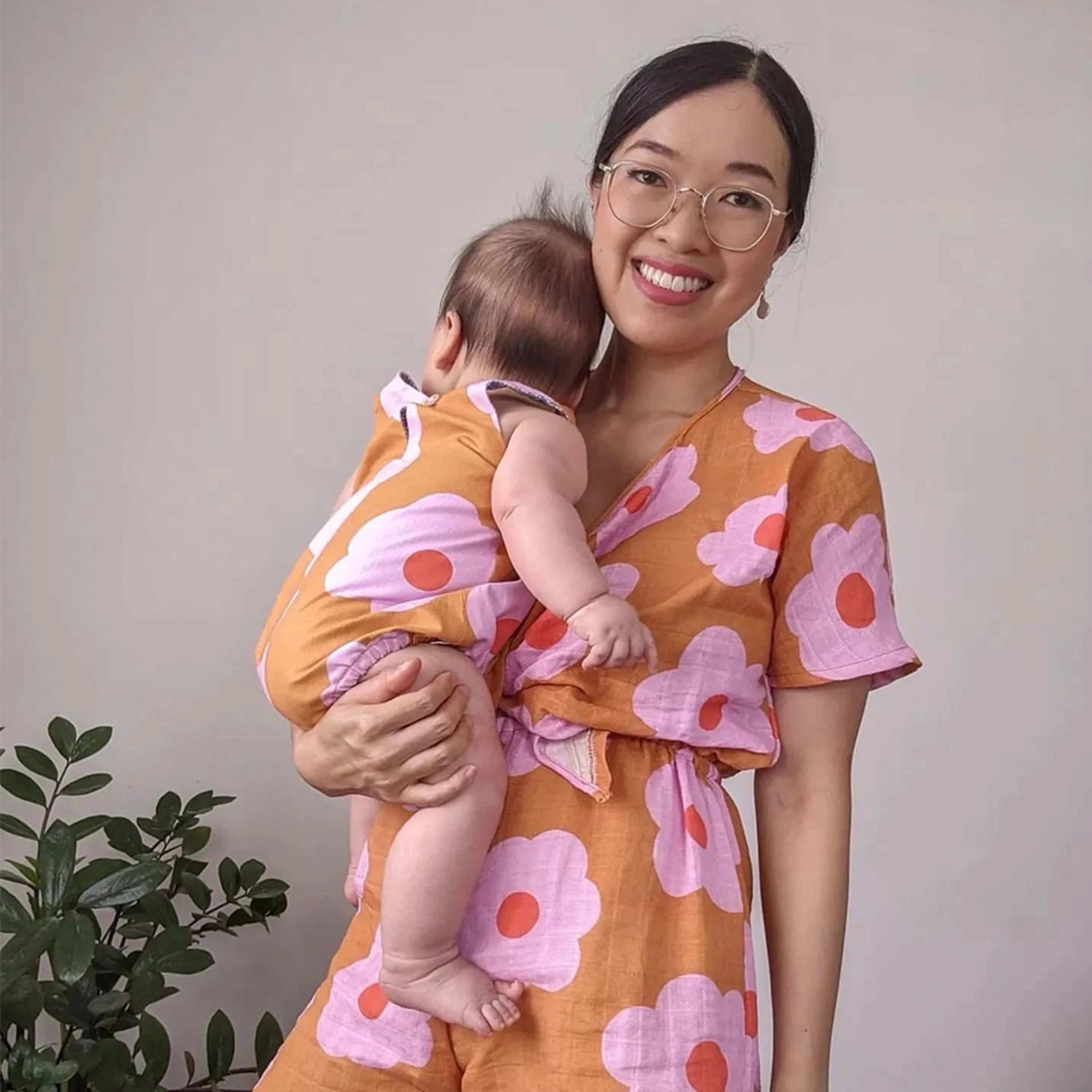 Woman in floral matching set holding baby wearing a onesie with the same pattern.